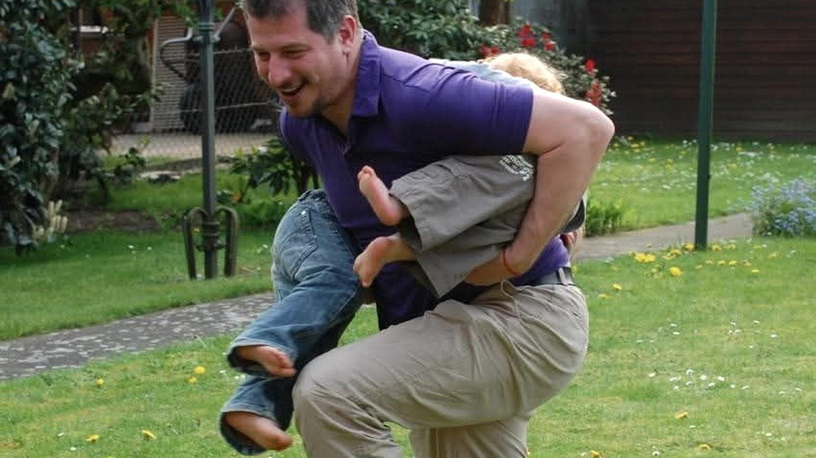 Eric Rainer trägt lachend ein Kind huckepack im Garten.